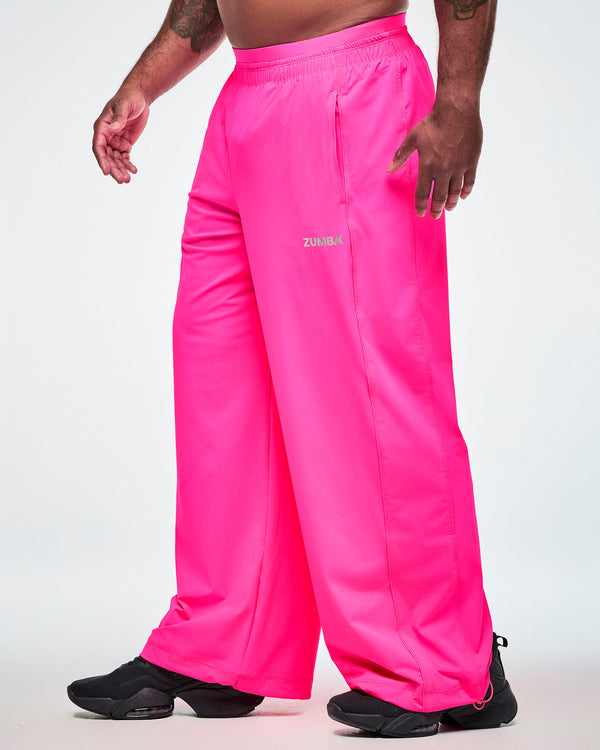 Side view of pink slouch pants worn by a male model, showing the elastic waistband, side pockets, and a small silver ZUMBA text on the upper left thigh.