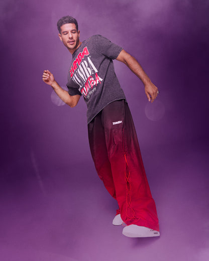 A male model wearing a black graphic tee paired with red-to-black ombre gradient pants dancing against a purple studio backdrop with a hazy, smoky effect.