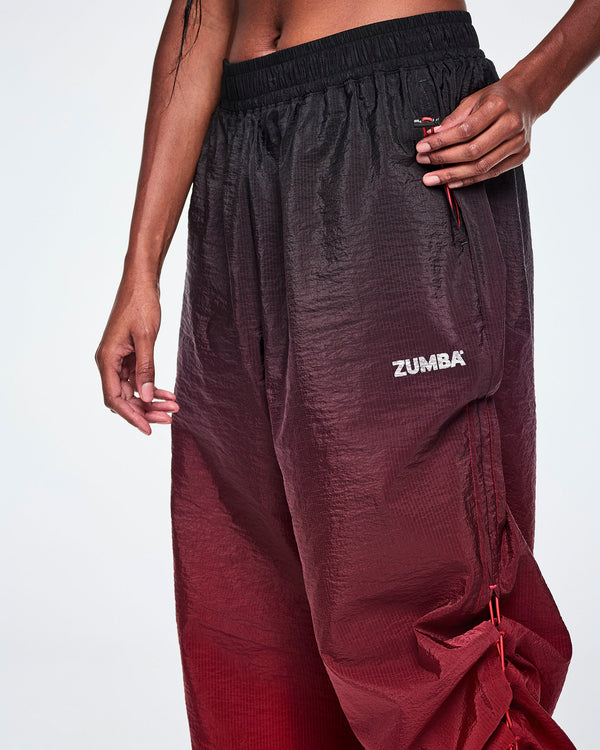 A close-up of a female model pulling on the bungee cord toggle in the pocket to adjust length of black to red gradient pants.