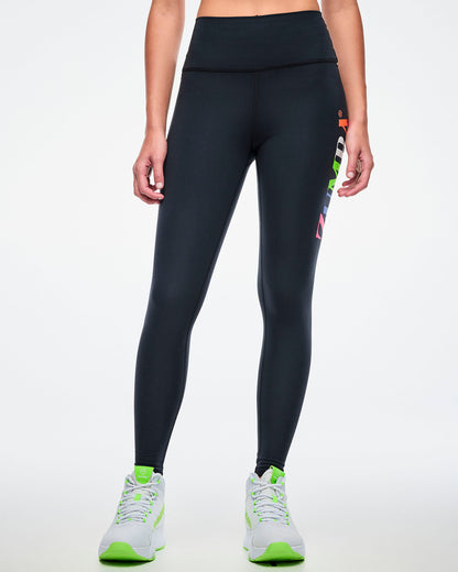 Front view of a female model wearing black Zumba leggings paired with green-and-white shoes.