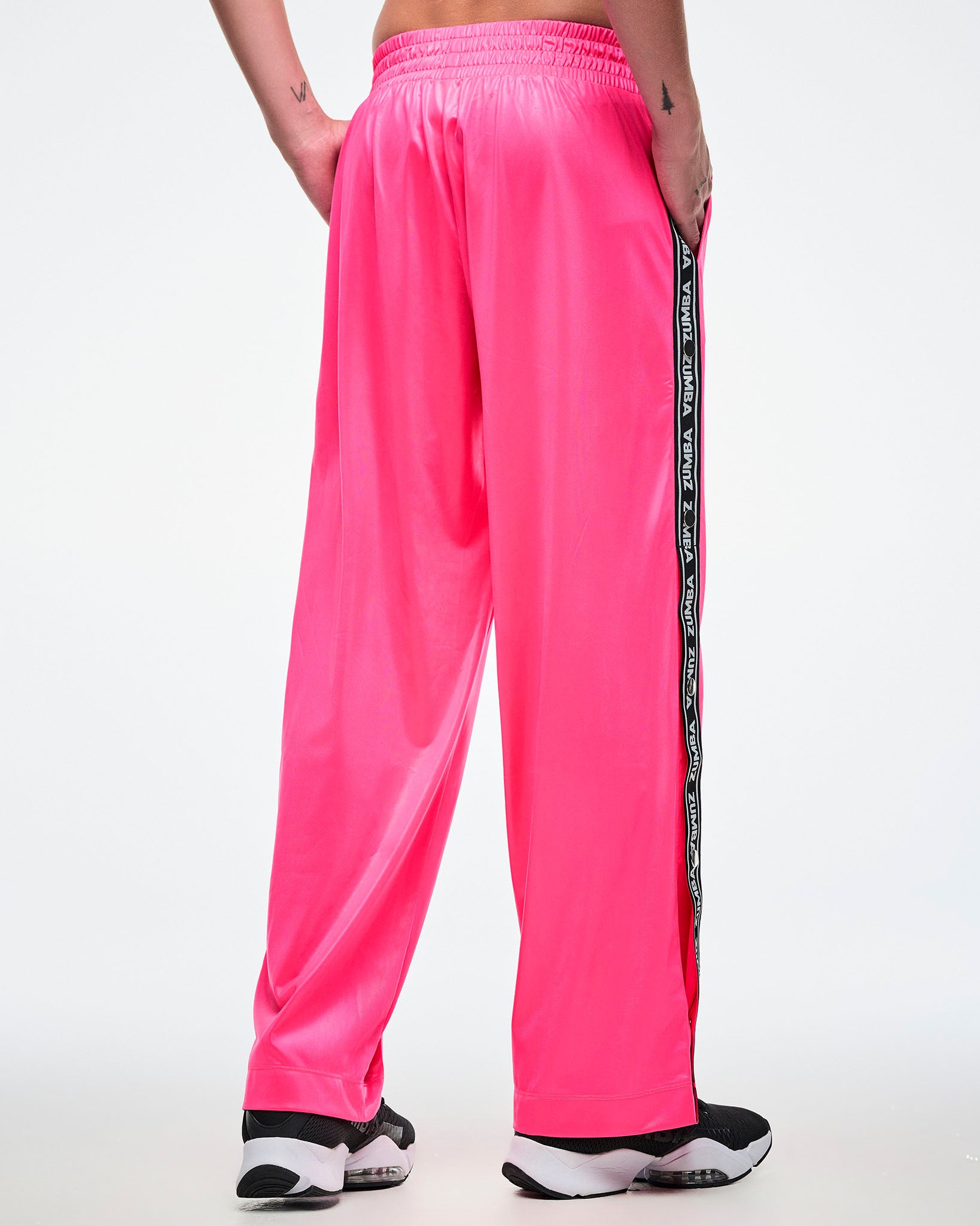 Back view of a male model wearing pink track pants with a black and white Zumba side stripe on a white background.