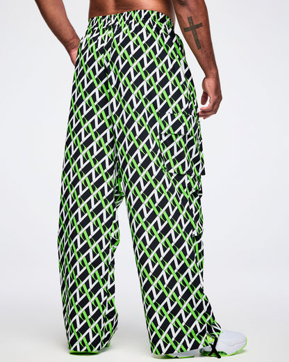 Back view of a male model wearing black cargo pants with an allover black, white and green “Z” crisscross pattern, left hand in his pocket, paired with black-and-white shoes.
