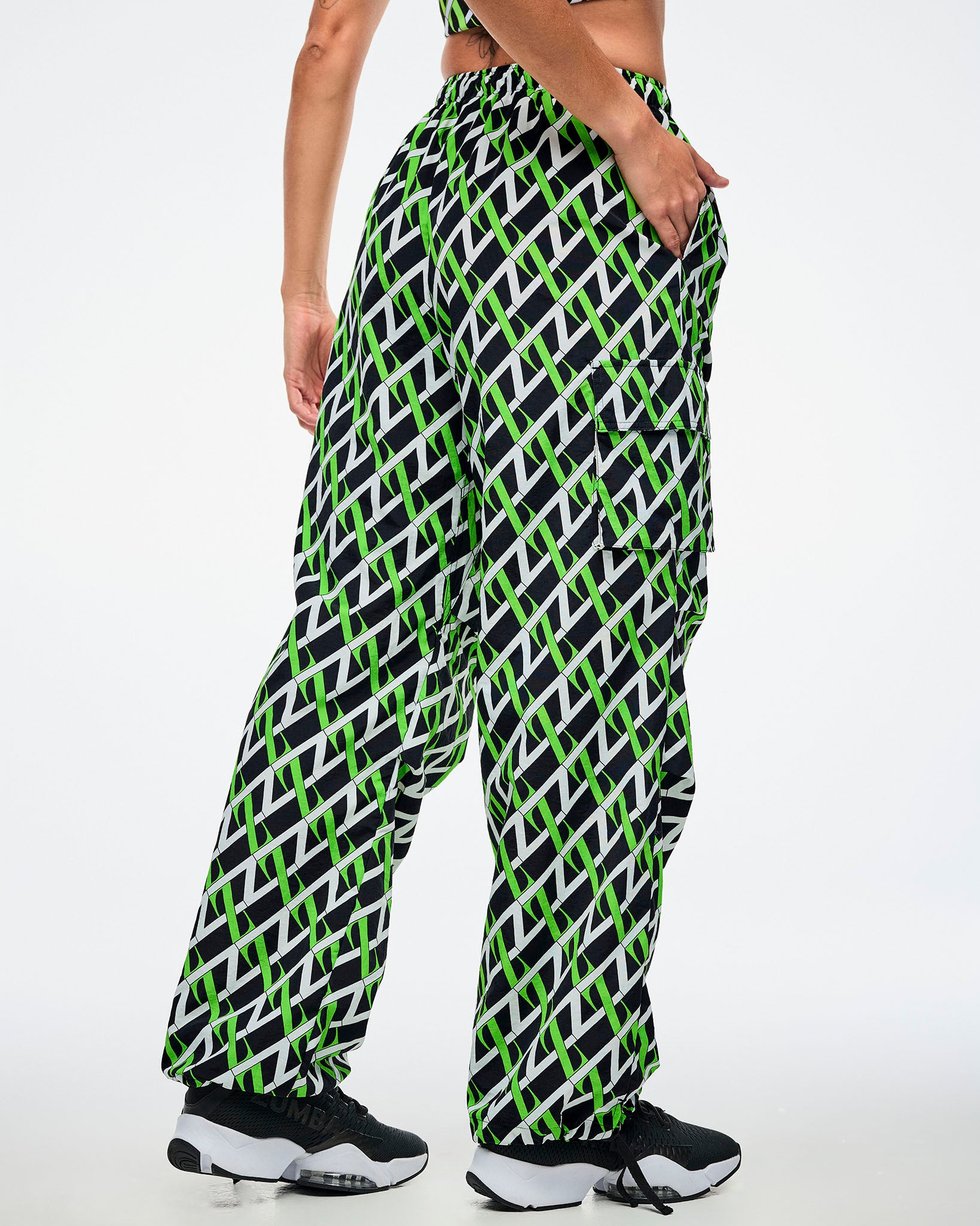 Back view of a female model wearing cargo pants with an allover black, white and green “Z” crisscross pattern, left hand in her pocket, paired with black-and-white shoes.