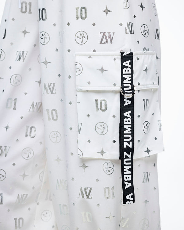 Close-up of the cargo pocket with a black‑and‑white “Zumba” ribbon, set against the silver Zumba motif print.