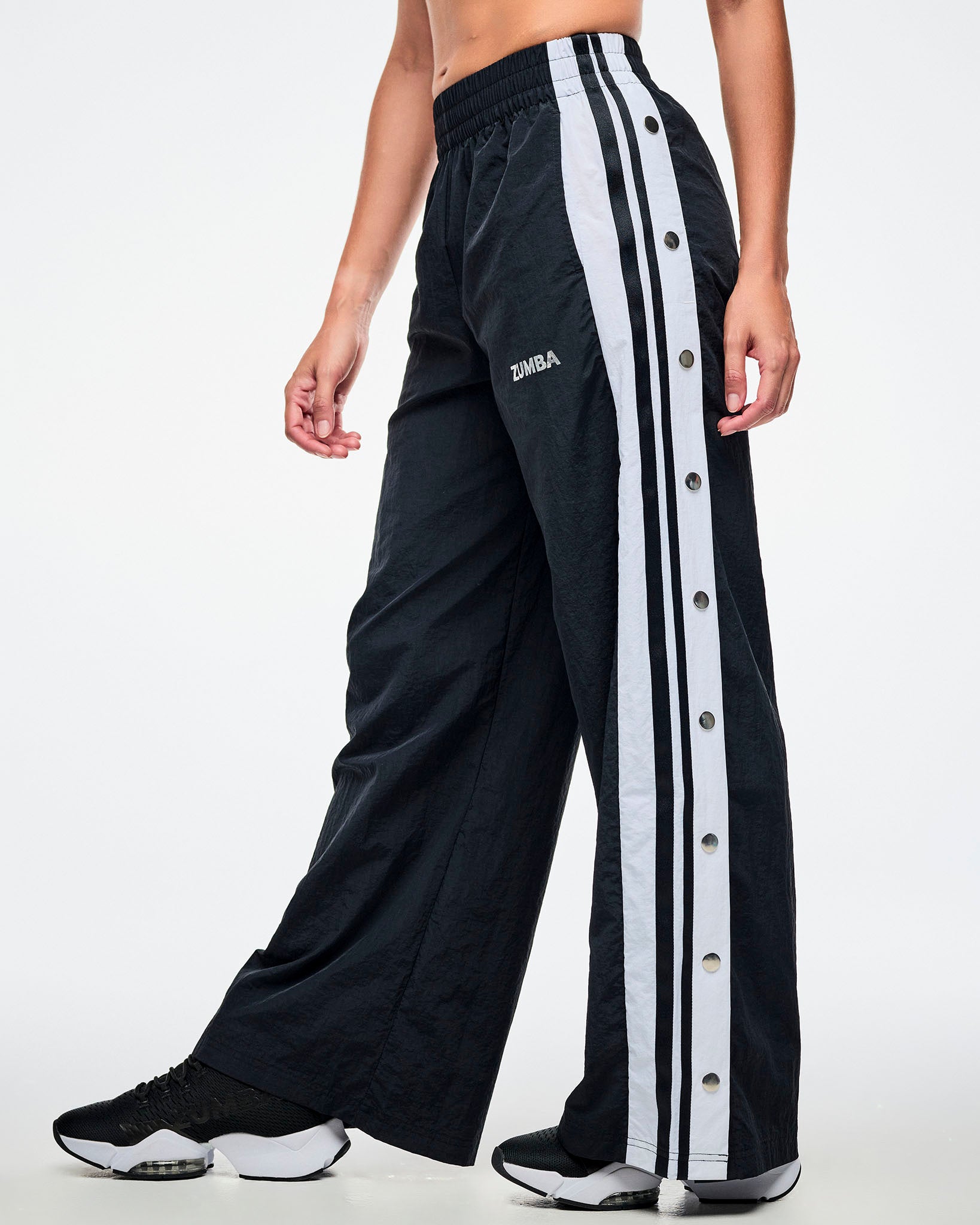 Female model wearing black pants with white stripes on the side with side snaps and paired with black and white shoes.