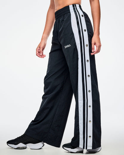 Female model wearing black pants with white stripes on the side with side snaps and paired with black and white shoes.
