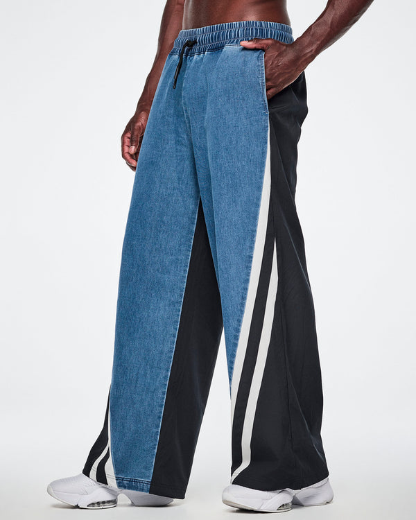 Side view of a male model wearing denim combo pants, showing the denim front, black back material, and striped side panel with an inseam pocket.