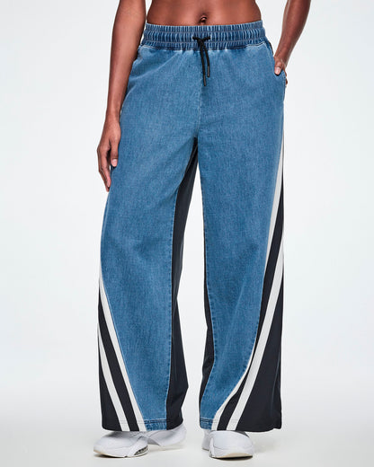 Front view of a female model wearing wide-leg denim combo pants with a black-and-white striped panel down each side, paired with white sneakers.