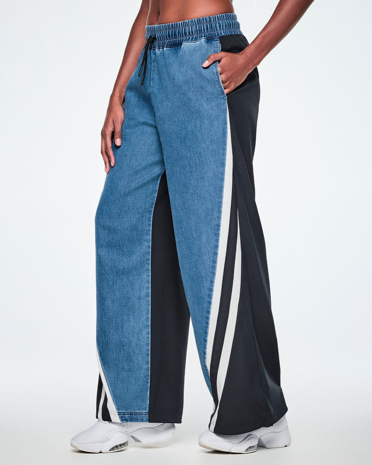 Side view of a female model wearing denim combo pants, showing the denim front, black back material, and a black-and-white striped panel along the side.