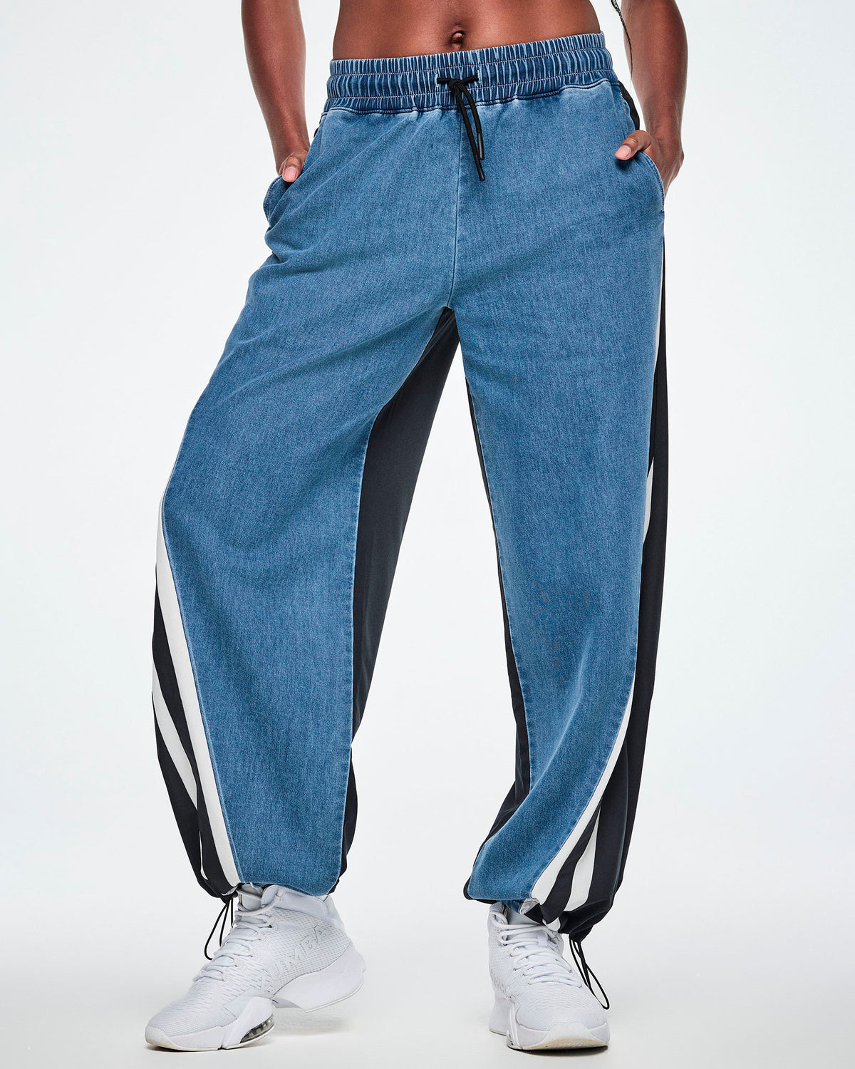 Front view of a female model wearing denim combo pants with an elastic waistband and drawcord, paired with white shoes.