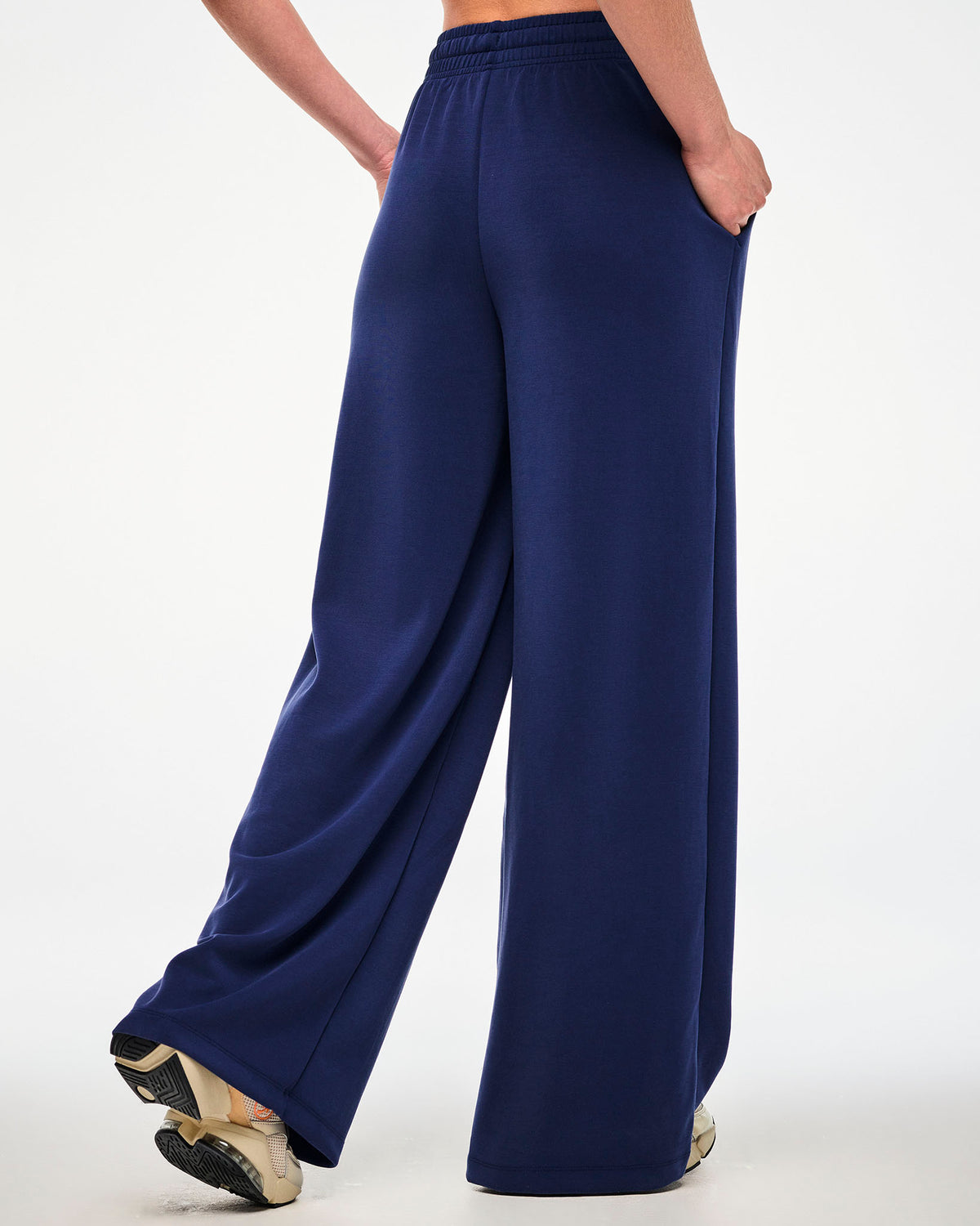 Shown from the back, a female model wears the navy high-waisted pants with an elastic waistband and a loose, full-length fit.