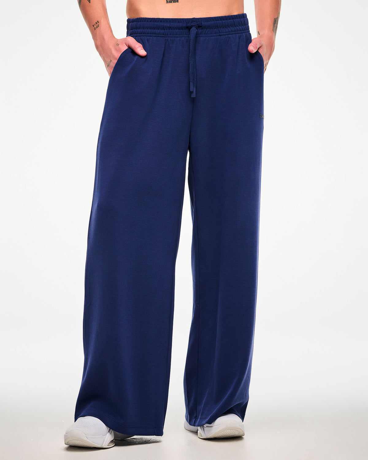 Male model in navy high-waisted pants with a drawcord waist, both hands in the side pockets and paired with white shoes.