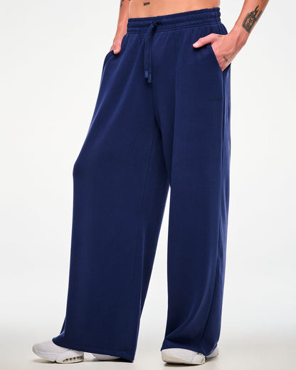 Male model in navy high-waisted straight-leg pants, turned slightly to show the wide leg, paired with white shoes.