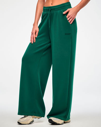 Female model in the teal green high-waisted pants, turned slightly to show the relaxed straight leg falling over beige shoes.