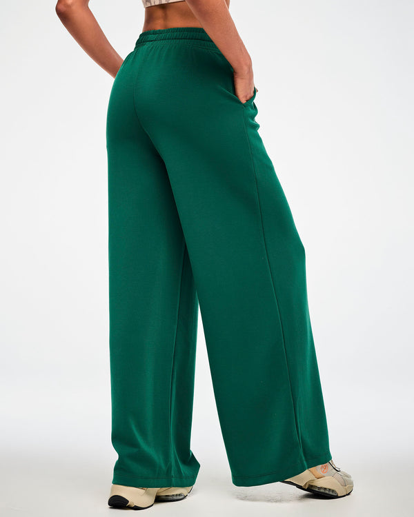 Back view of a female model in teal green high-waisted straight-leg pants, showing the elastic waistband and full-length wide legs, paired with beige shoes.