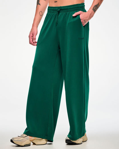 Male model in the teal green high-waisted pants, turned slightly to show the wide, relaxed leg, paired with beige platform shoes.
