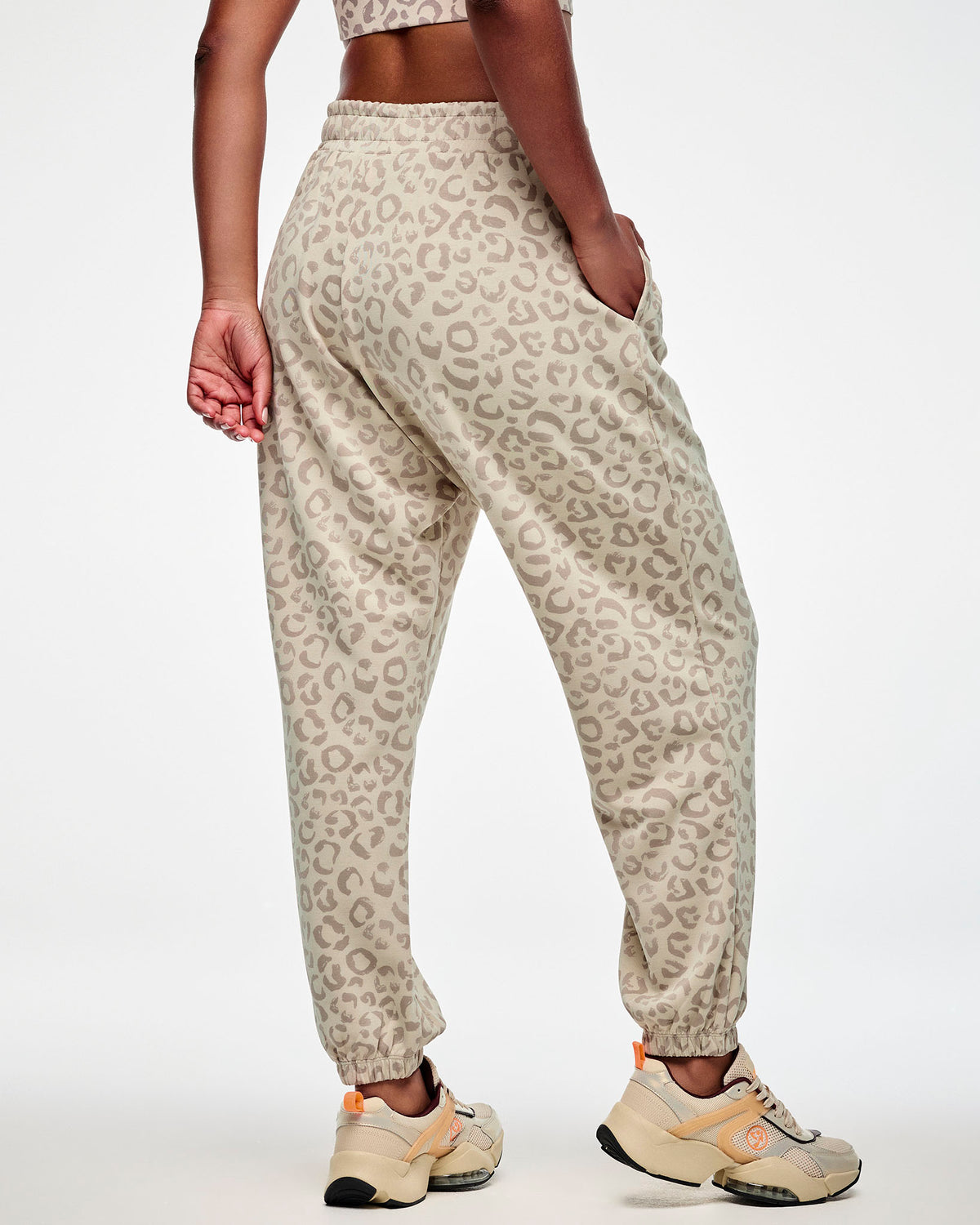 Shown from the back, a female model wears the beige leopard print slouch cargo pants with a loose fit through the seat and elastic cuffs at the ankles.