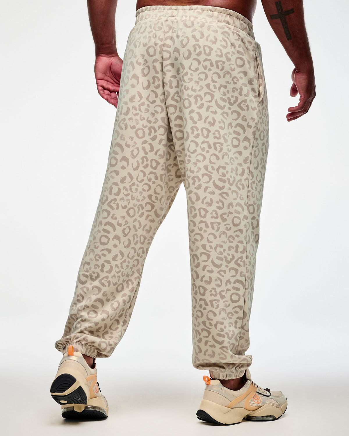 Back view of a male model in beige knit slouch cargo pants with a light brown leopard print, showing the relaxed fit and elastic cuffs at the ankles.