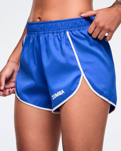 Blue Zumba shorts with white trim and small white Zumba text on the left leg worn by a female model.