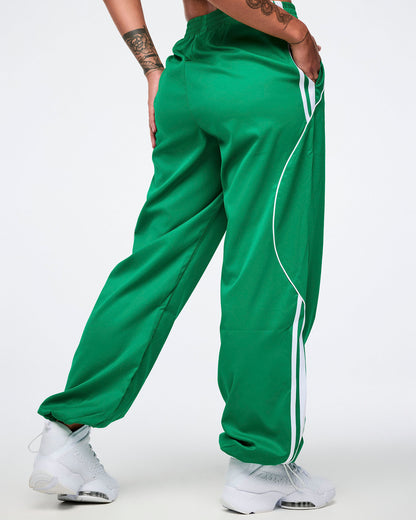 Back view of a female model wearing green Zumba curvy track pants with white stripes and white shoes.