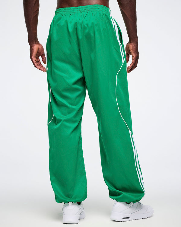 Male model posing with a back view of the green Zumba curvy track pants with white stripes.