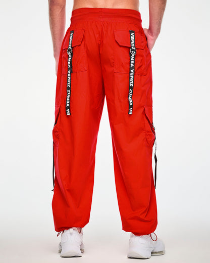 Back view of a male model in the red cargo pants, showing two back cargo pockets, each with a black 'ZUMBA' webbing strap hanging from a silver D-ring.