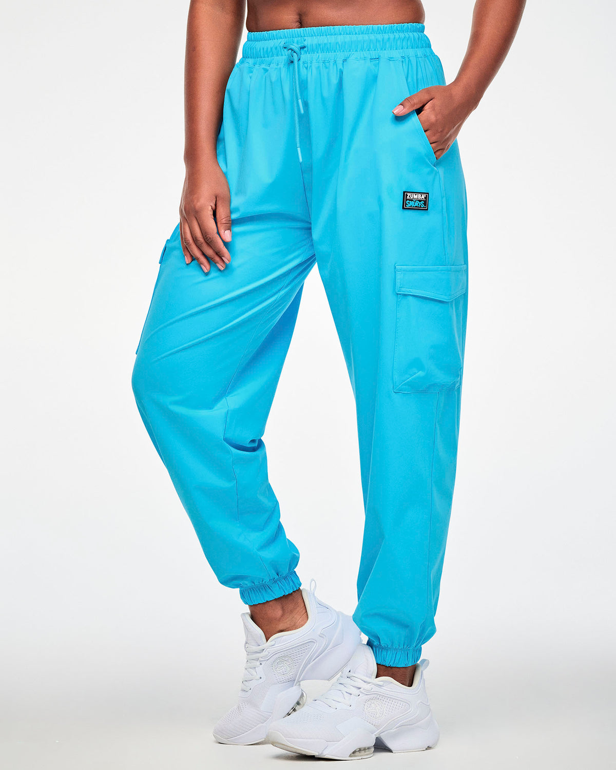 Female model in the aqua blue cargo pants, shown in side view with the relaxed leg tapering into elastic cuffs above white shoes.