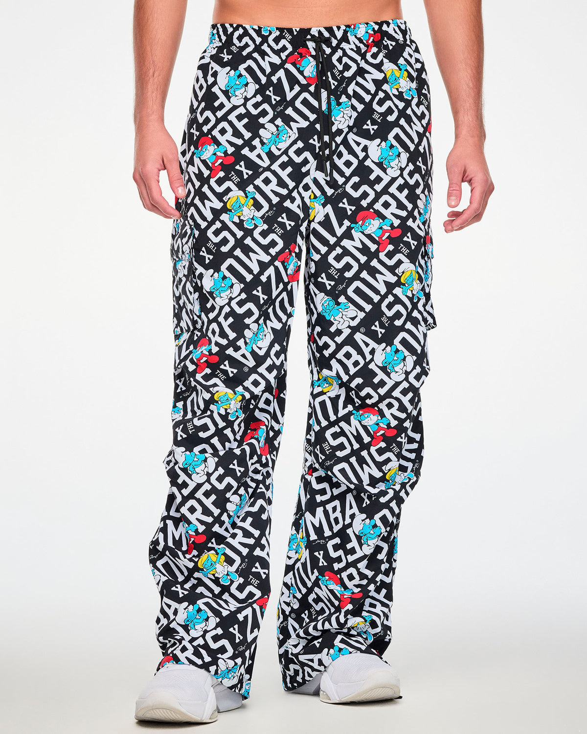 Male model in the black and white Smurfs print oversized cargo pants with a black drawcord waist and cargo pockets on both legs, paired with white shoes.