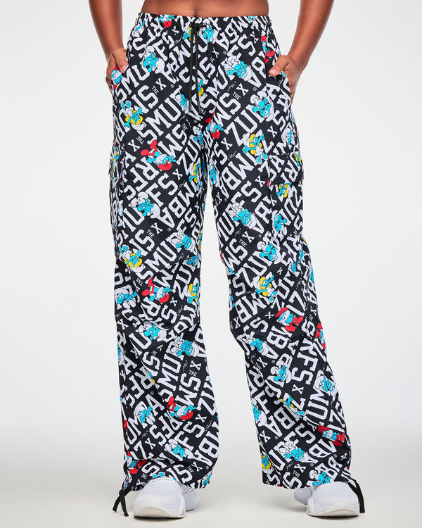 Female model with both hands in the pockets of the black and white Smurfs print cargo pants, with a black drawcord tied at the waist and black drawcords hanging at the hems.