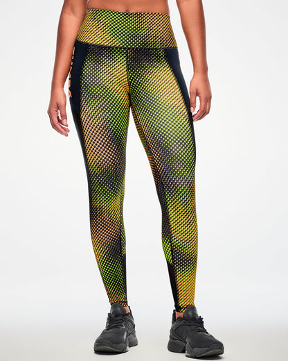 Female model wearing ankle leggings with a yellow and orange halftone dot gradient print and a mesh side panel and black shoes.
