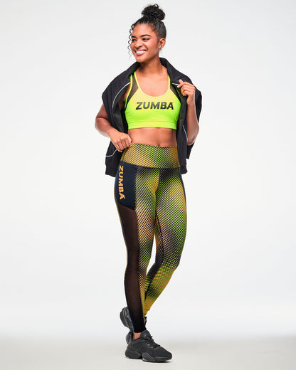 Female model wearing high-waisted ankle leggings with a yellow and orange gradient print, paired with a black jacket draped around her neck and black shoes.