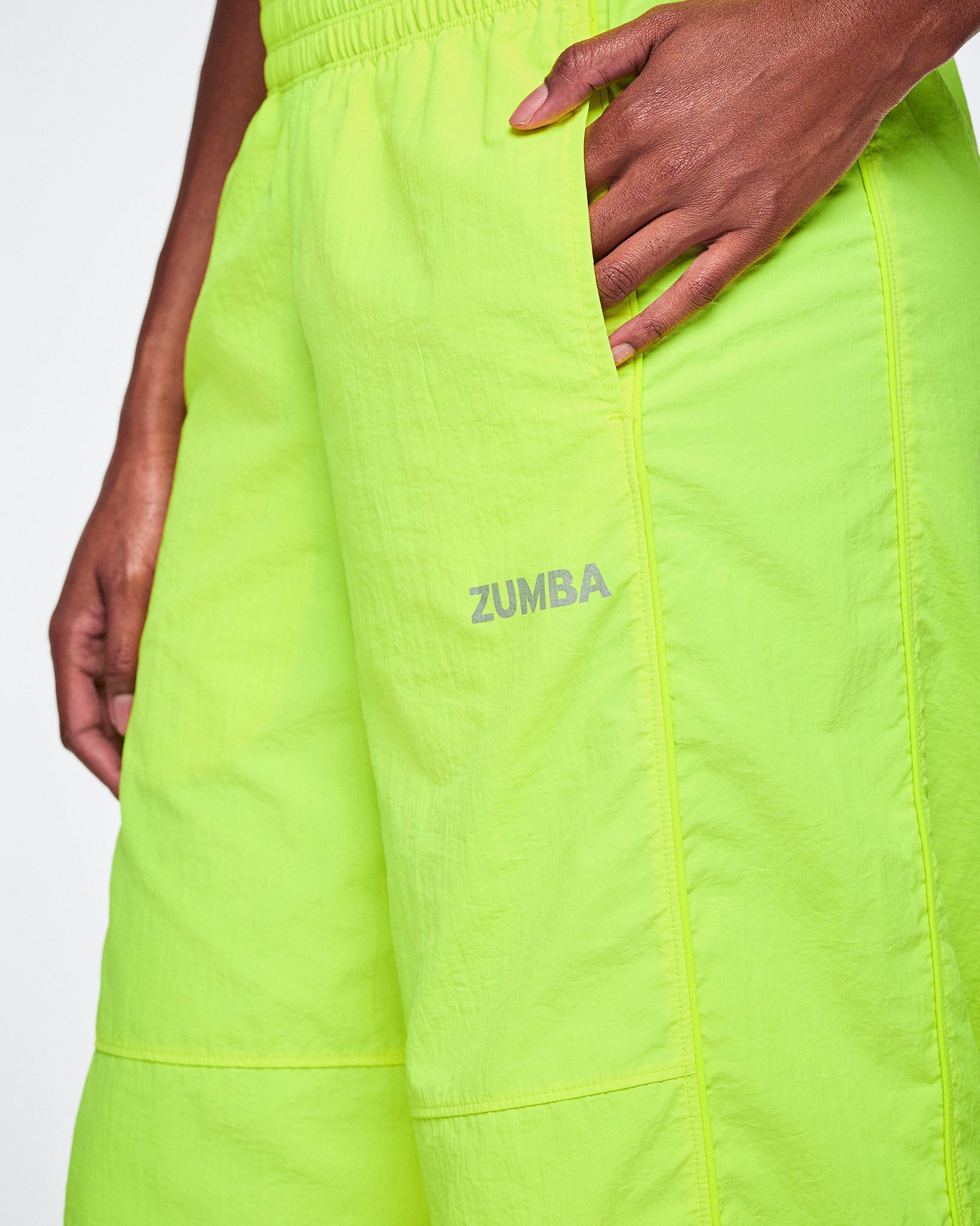 Close-up of neon yellow-green pants with a side pocket and the word ZUMBA printed in silver on the thigh, shown on a female model.