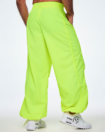 Back view of a male model wearing bright yellow-green Zumba pants with white shoes.