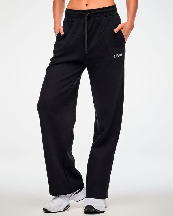 Female model wearing the black waffle-knit wide-leg track pants with both hands tucked into the side pockets.