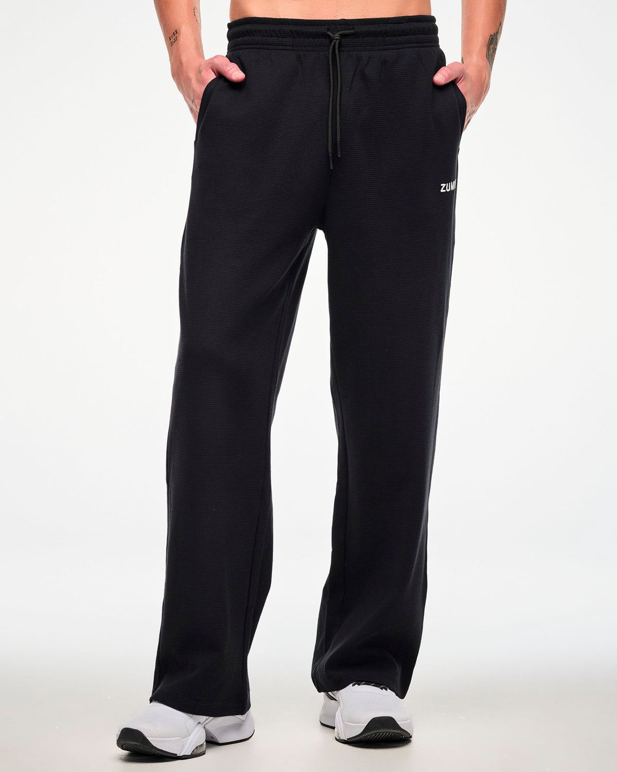 Front view of a male model wearing the black waffle-knit wide-leg track pants with both hands in the side pockets.