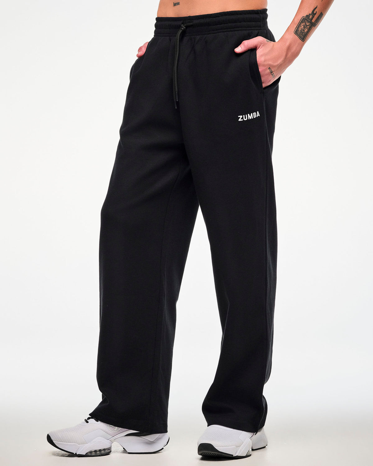 Male model in the black waffle-knit wide-leg sweatpants with white 'ZUMBA' text on the upper left leg and both hands tucked into the side pockets.