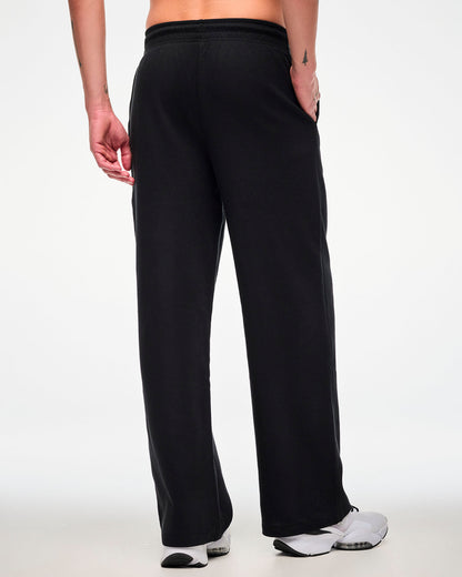 Shown from the back, the black waffle-knit track pants on a male model with one hand tucked into a side pocket.