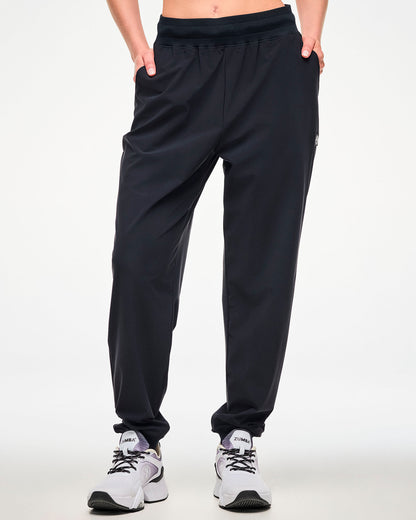 Front view of a female model wearing high waisted black jogger pants with hands in the side pockets and paired with white shoes.