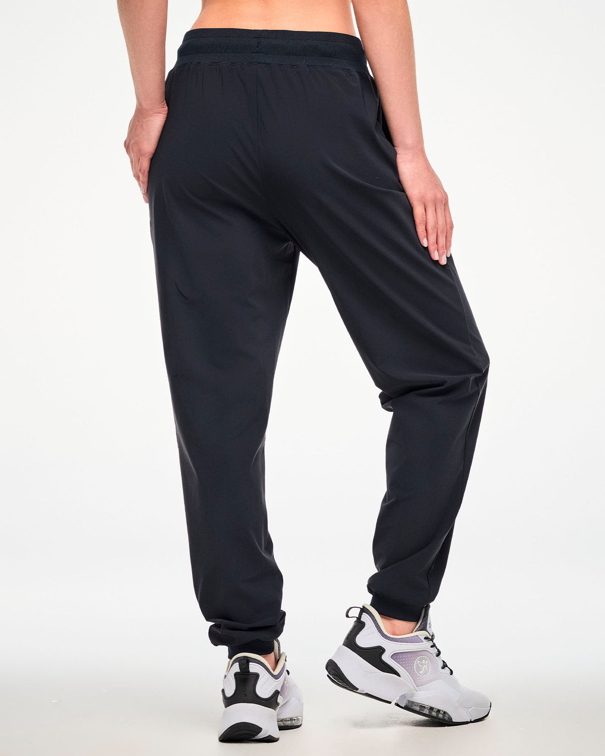 A female model shown from the back wearing high waisted black jogger pants and white athletic shoes.