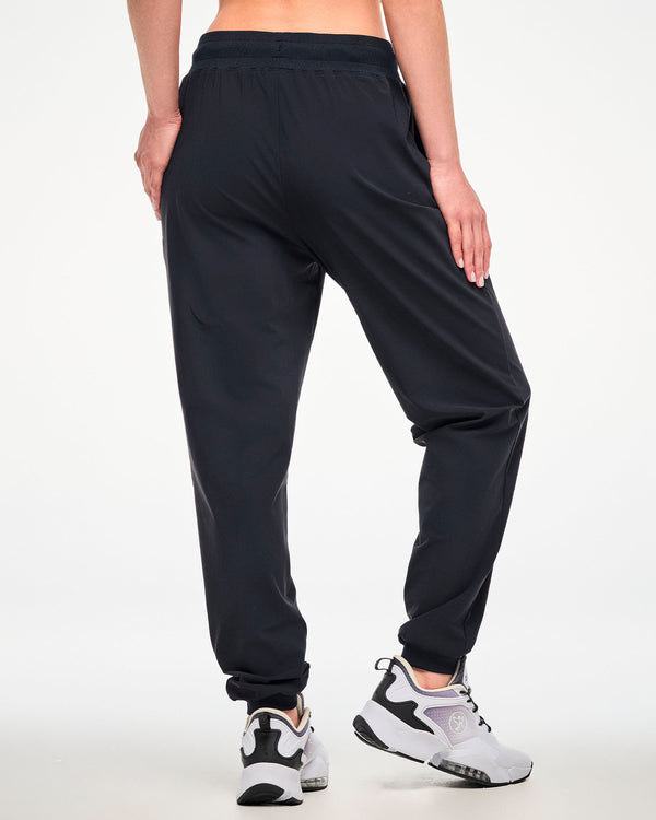 A female model shown from the back wearing high waisted black jogger pants and white athletic shoes.