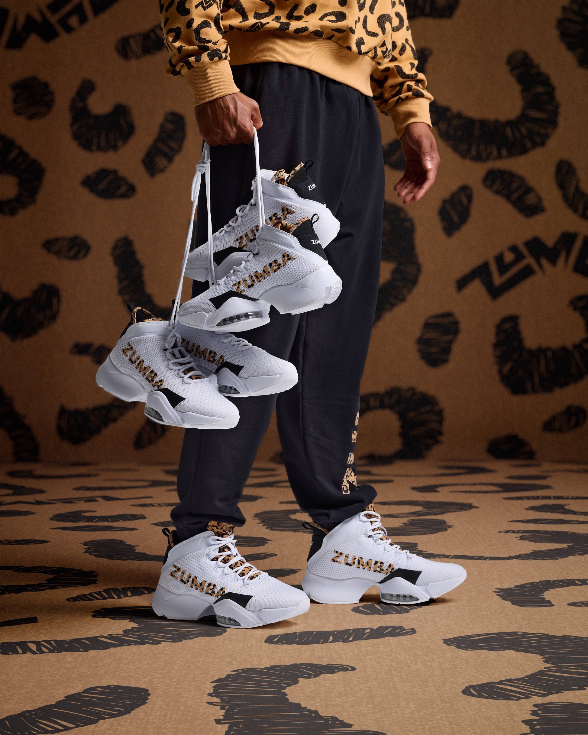 White high-top sneakers with leopard logo detail on male model in black joggers and a tan leopard print sweatshirt.