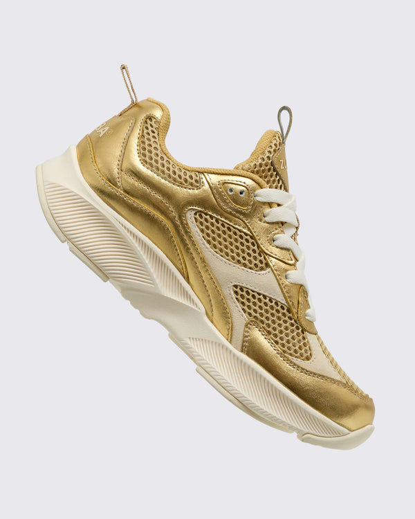 Side angled view of the gold Zumba shoe with laces and back pull tab on a light background.