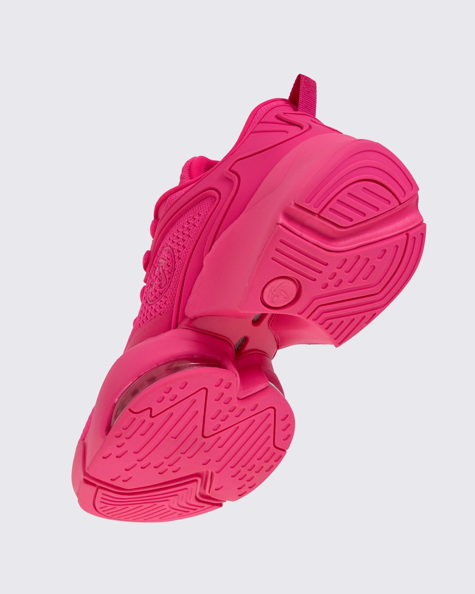 Left angled underneath view of a pink shoe with a pink Zumbito showing more of the pink sole against a white background.