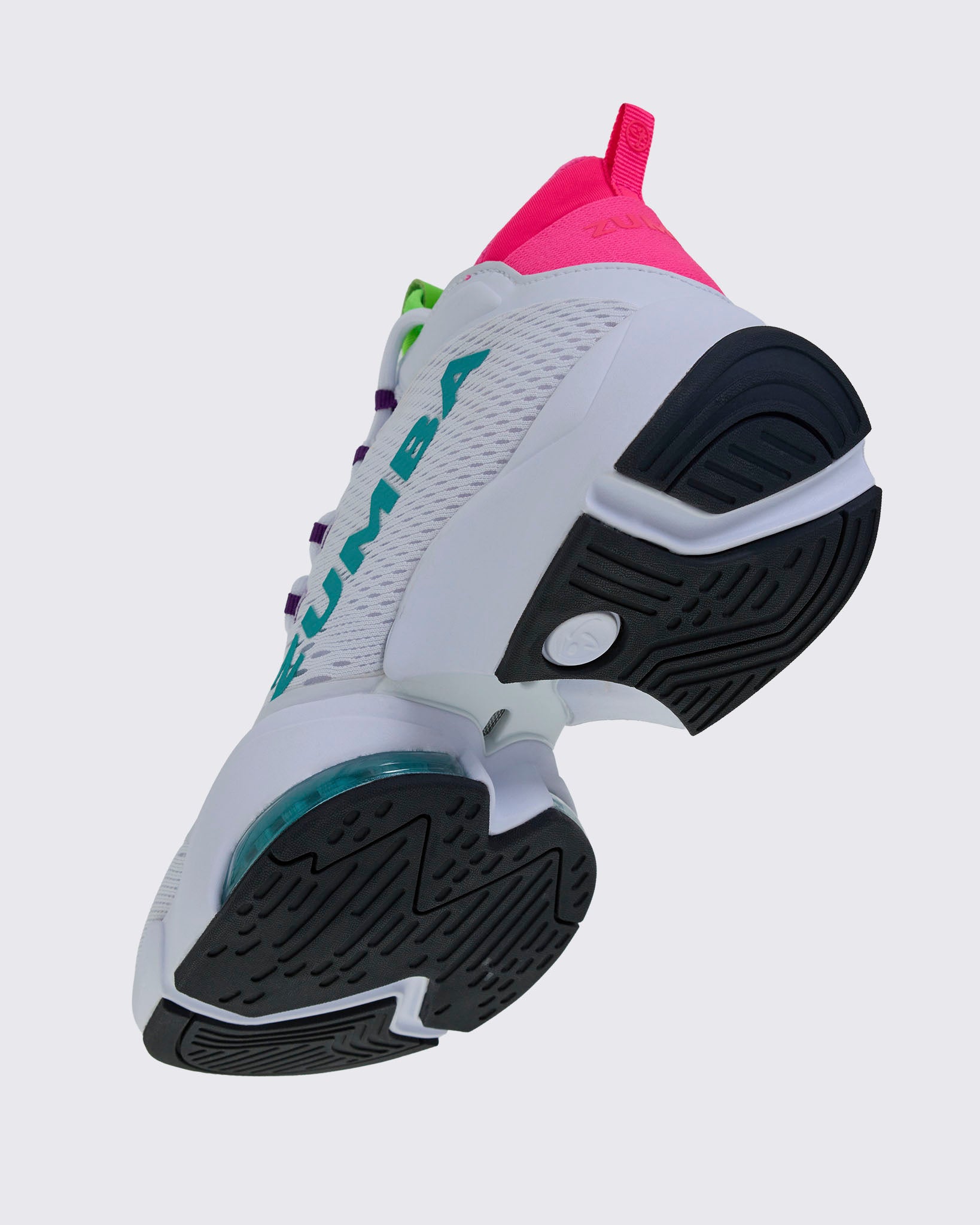 Angled underside view of a white sneaker showing the textured black outsole and aqua "ZUMBA" text along the side, with pink and green heel tabs.