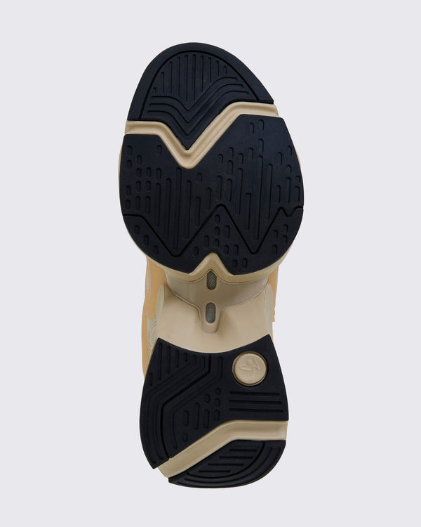 Sole view of a beige platform shoe with black rubber tread on the forefoot and heel, a beige split midsole with small arch windows, and a round Zumbito medallion in beige at the heel.