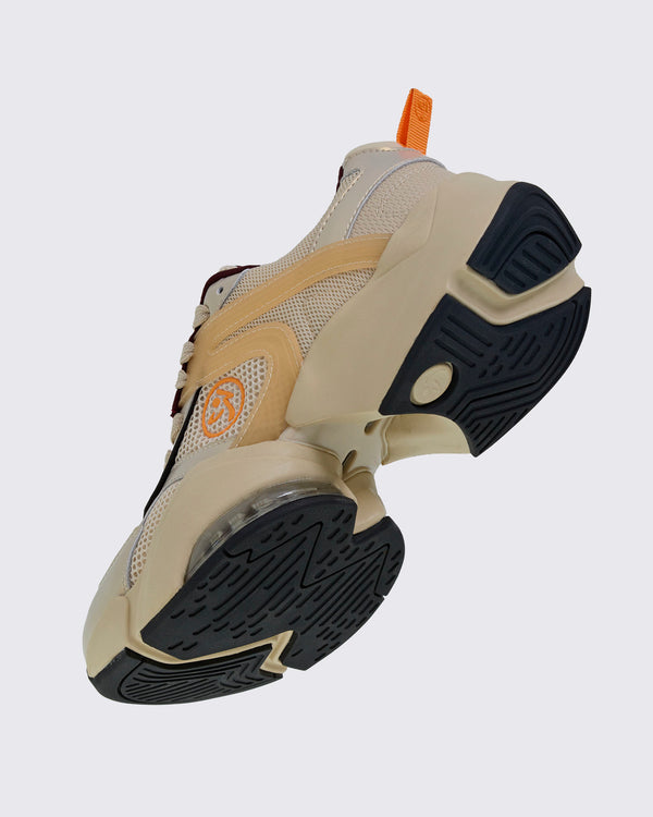 Angled underside view of a beige platform shoe, showing black rubber tread on the split sole, a round Zumbito medallion near the heel, and an orange Zumbito logo on the side.