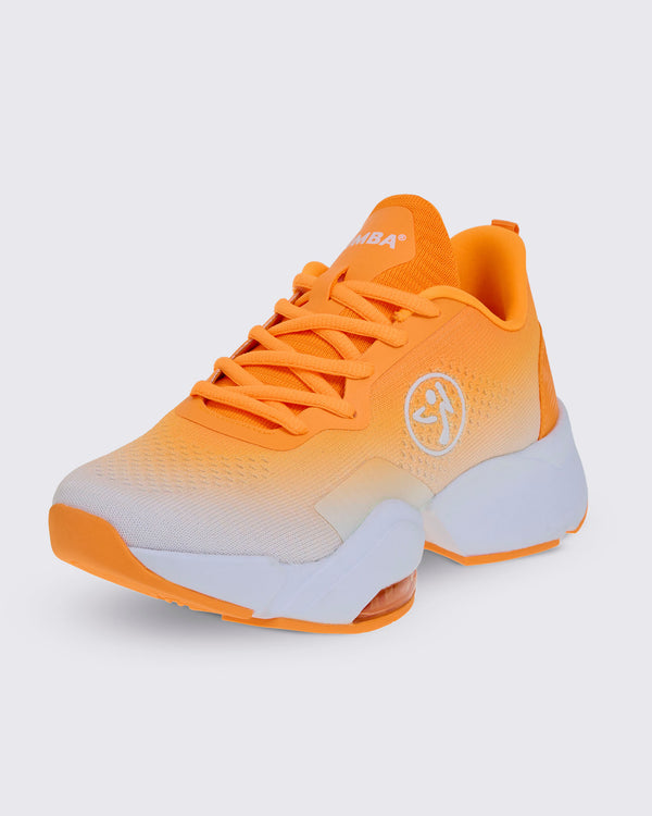 Front side view of an orange lace-up shoe with a knit upper that fades from orange to white at the toe, a white Zumbito logo on the side, white 'ZUMBA' text on the tongue, orange laces, and a chunky white split sole.