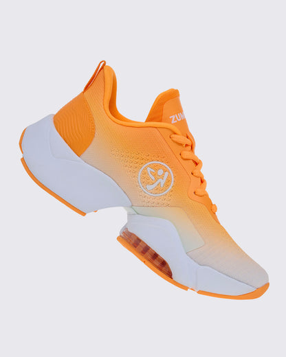 Right side view of the shoe, with orange laces, a white Zumbito logo on the ombre knit, an orange heel pull loop, and a chunky white sole that dips under the arch.