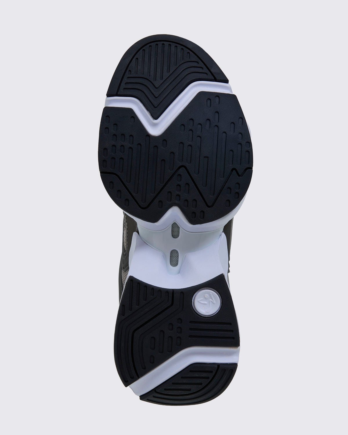 Sole view of the shoe, showing black grooved rubber tread split into forefoot and heel sections on a white sole, with a white Zumbito logo disc at the heel.