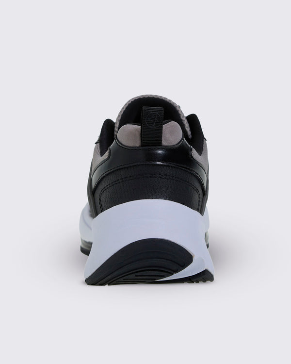 Heel view of the shoe, with a black perforated heel panel, a black pull tab with a Zumbito logo, grey lining, and a thick white sole over black tread.